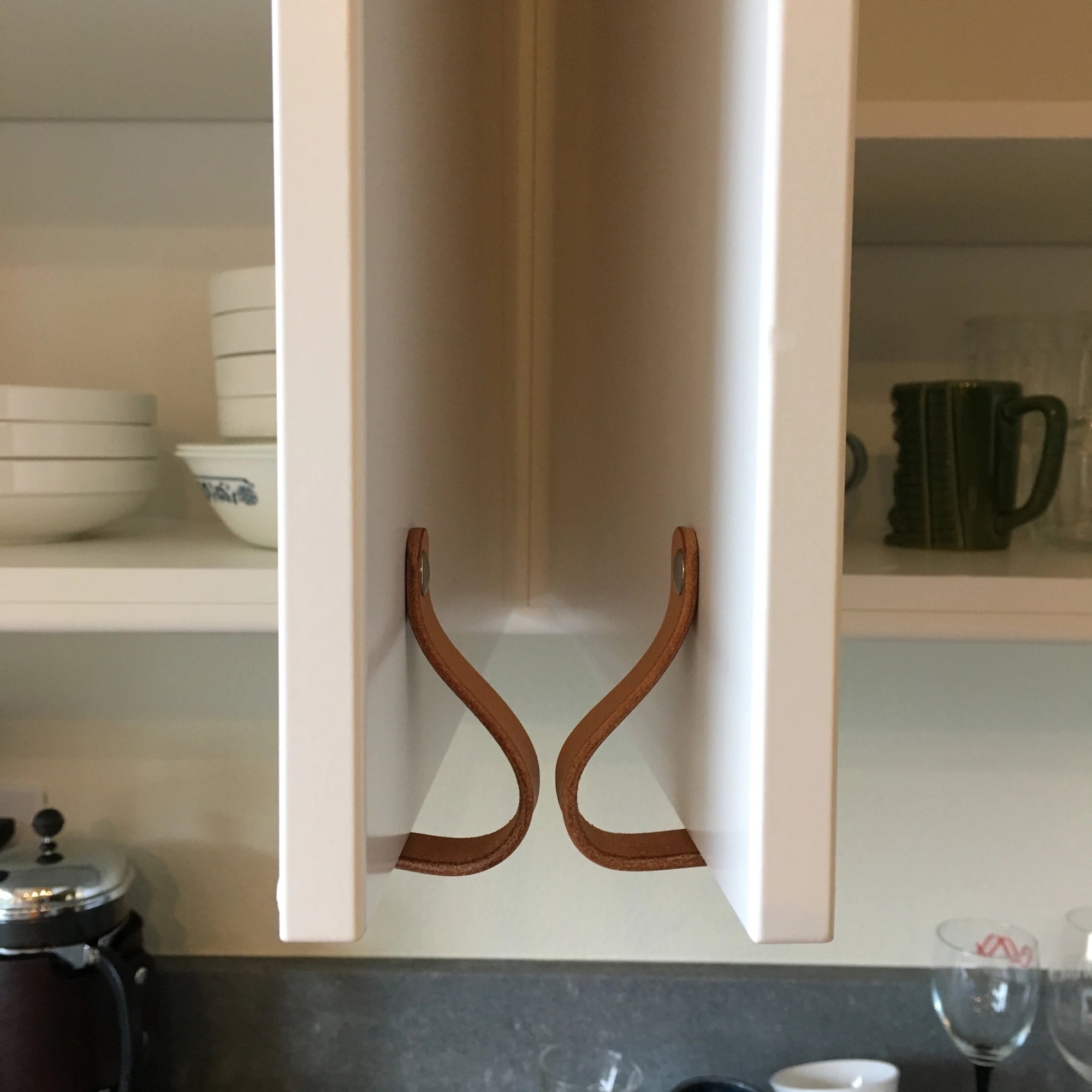 Two cabinet doors swinging open towards each other with matching leather Lovejoy loop handles. The leather touches so the cabinets don't crash into each other, a solution for problem corners in kitchen design planning