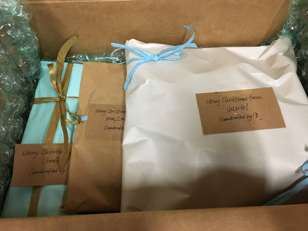 A set of three gift-wrapped presents in a box, each with a different plain-colored wrapping and each with a different gift note