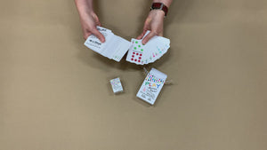 Video of a woman taking the poker-size travel domino playing cards out of the box, and running them through her hands to show how many cards there are (92+). Then she picks up the domino-sized cards and does the same. Both cards and both boxes are on the same table next to each to compare sizes.