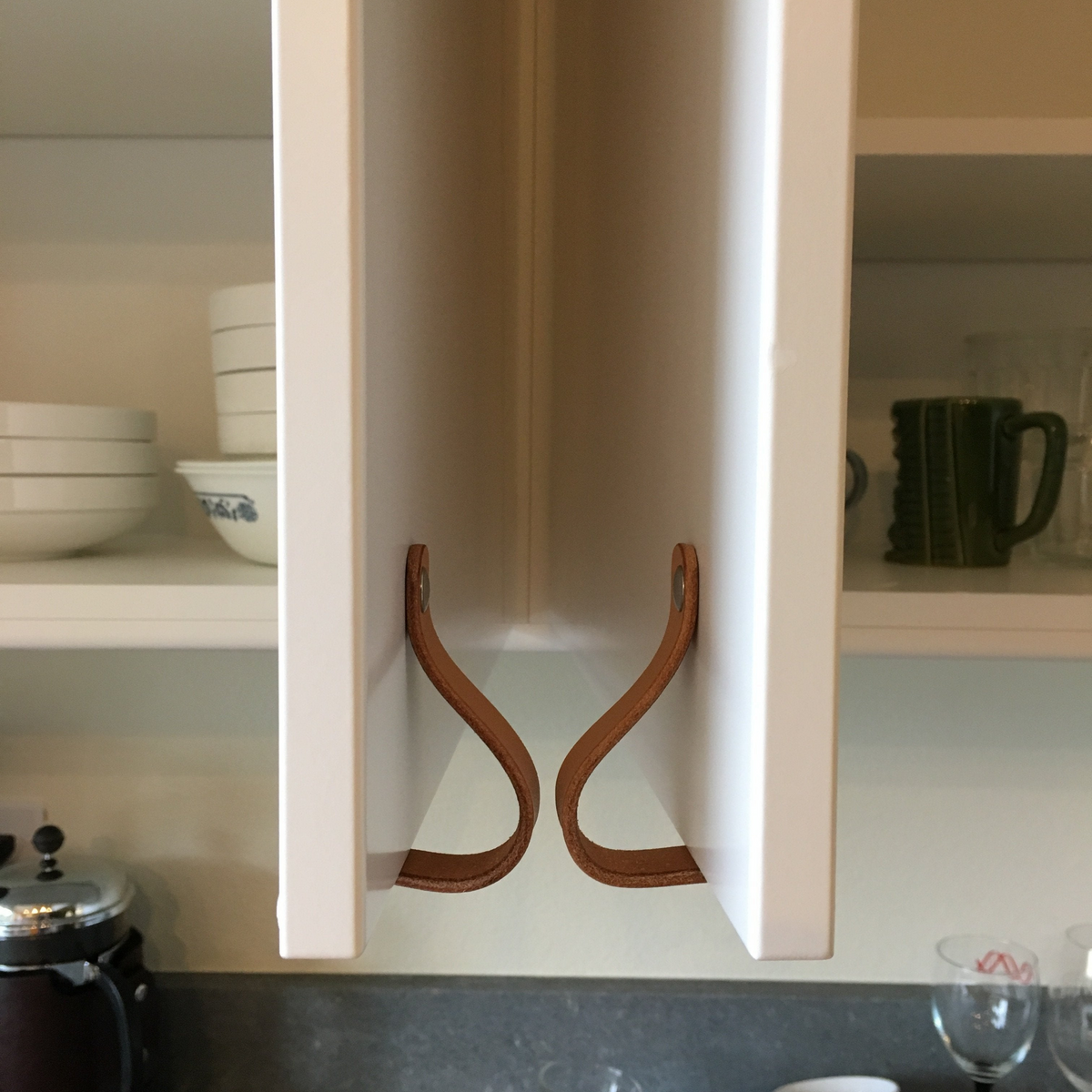 Two cabinet doors opening onto each other with leather handles. The picture shows that the leather handles hit each other first, which act as a bumper and prevents gouging in awkward corners. 