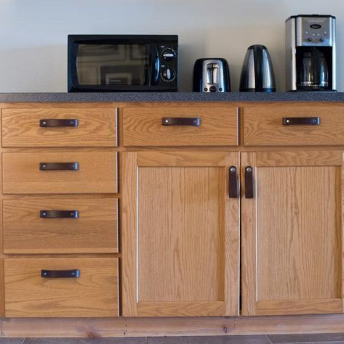 AirBnB kitchenette with oak wood cabinetry and dark brown leather handles.