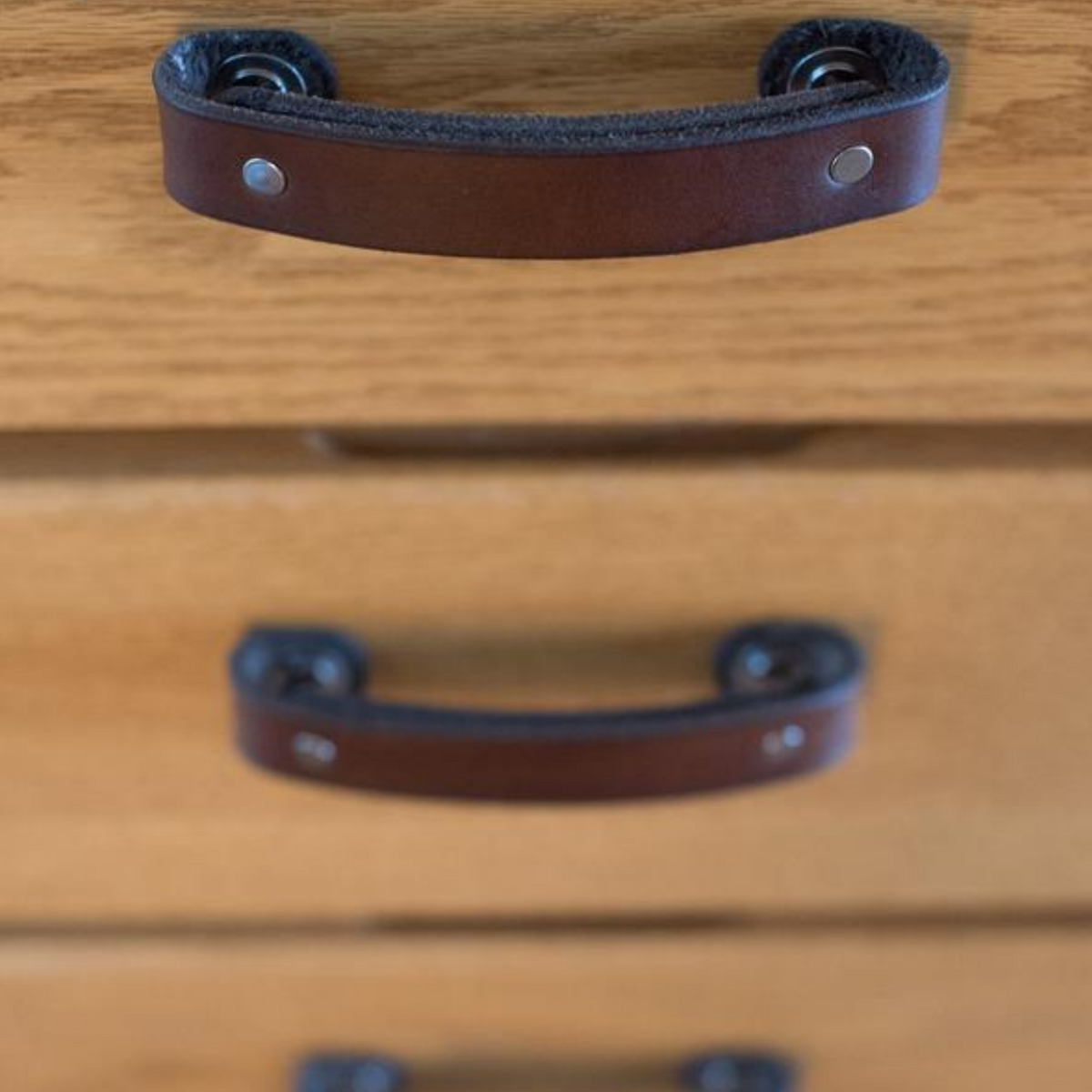 Close-up photo of Dark Brown leather handles with Nickel hardware seen looking downwards at an angle to show the projection off the cabinet surface. 