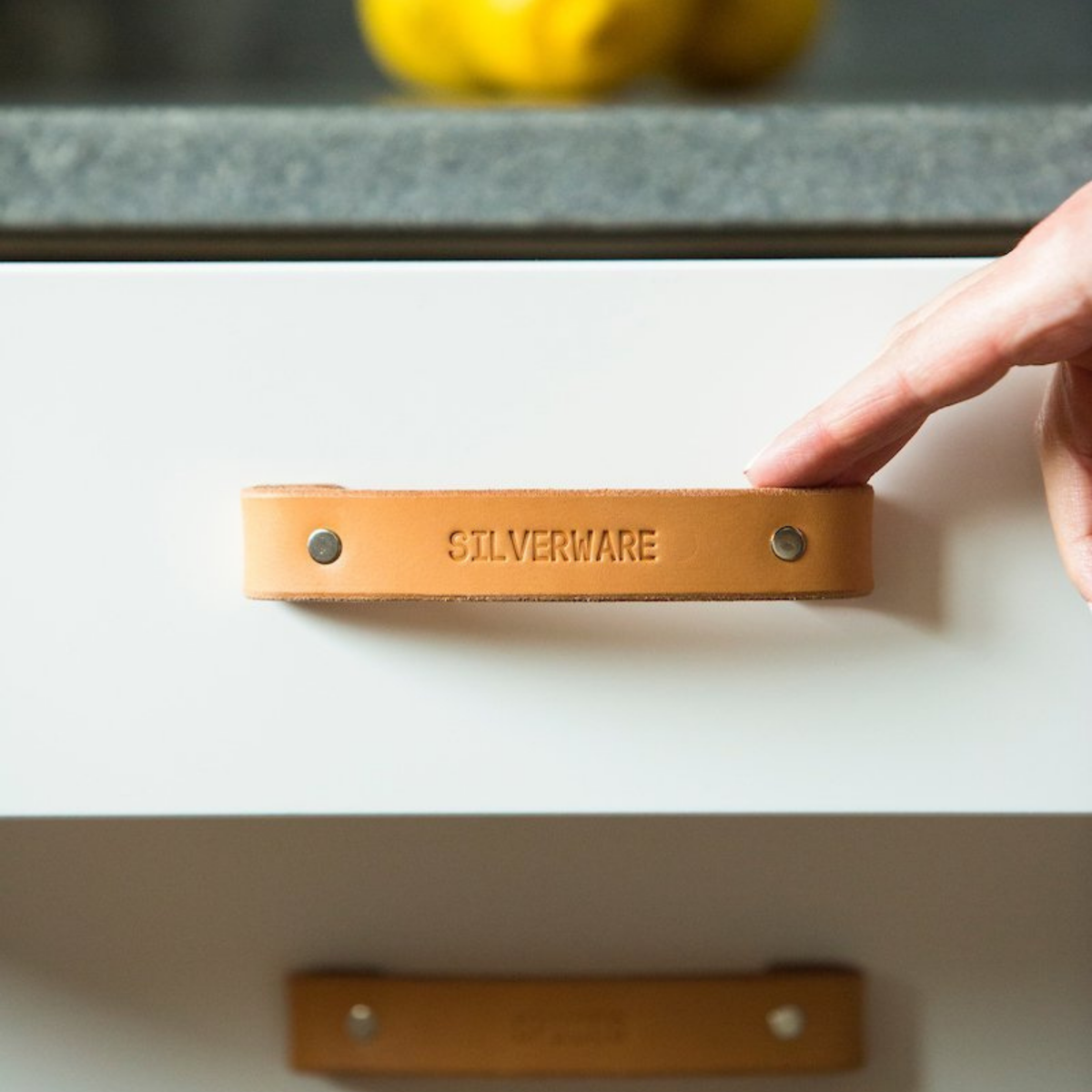 Close-up photo of a Natural un-dyed vegetable-tanned leather Tilikum handle with a custom message debossed into the surface identifying it as the silverware drawer. 
