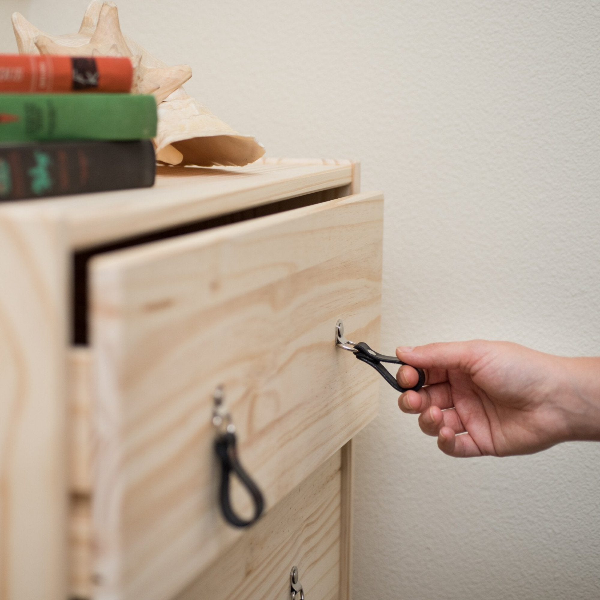 Woman's hand reaching out to an IKEA knotty pine wood dresser drawer and pulling it open using a small leather hinged handle in black leather with nickel hardware. 