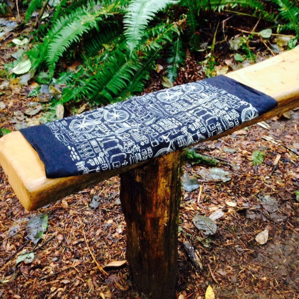 Bike print bandana folded into thirds and laid flat over a wooden bench on the forest floor
