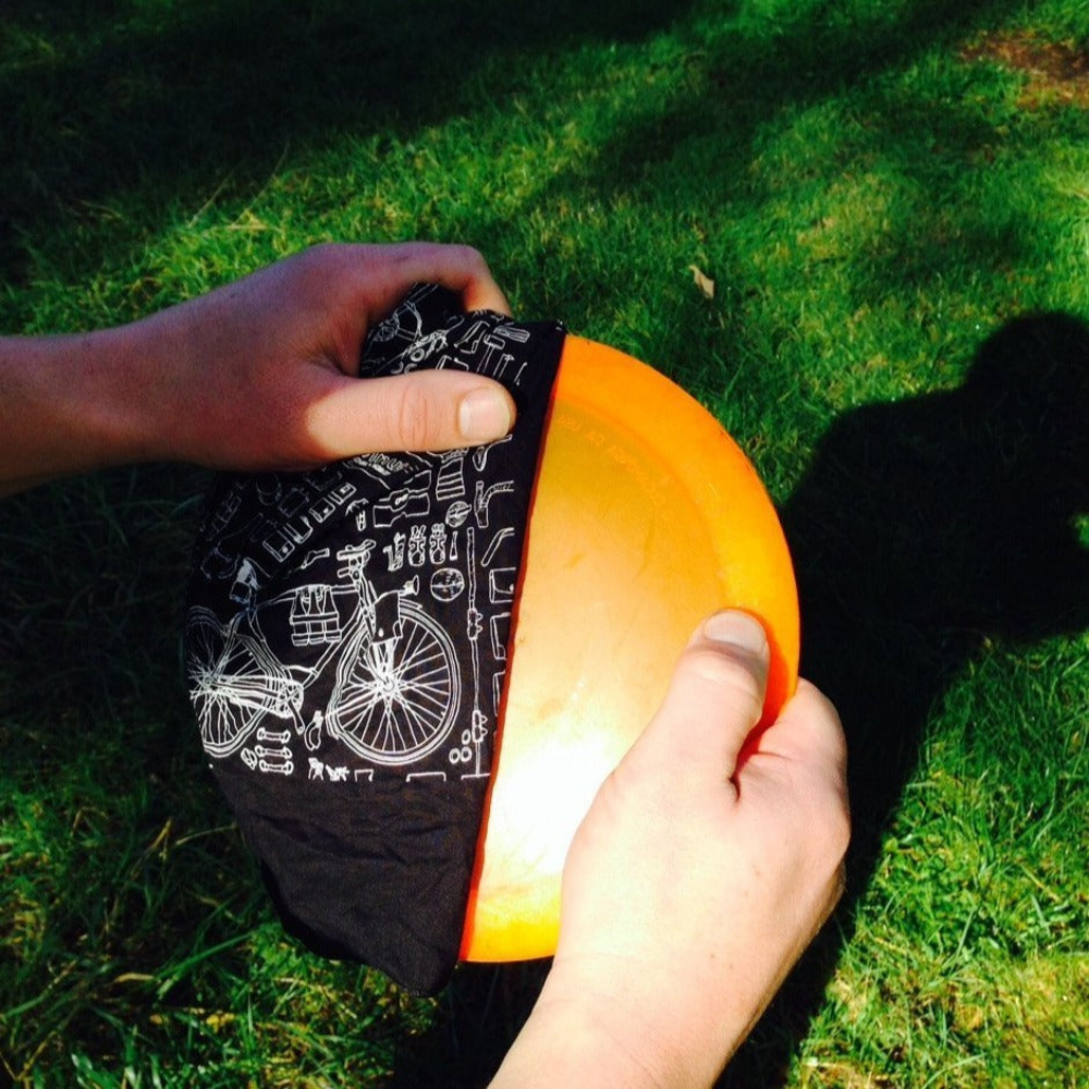 Two hands holding a black print bicycle bandana wrapped around an orange dic