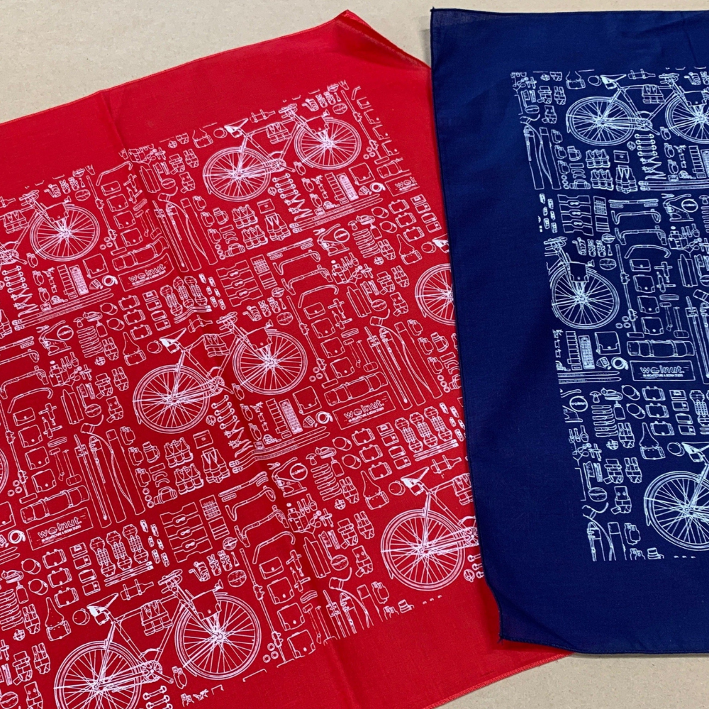 Red and blue bicycle print bandana laid side-by-side for comparison. Both bandanas are printed in white technical blueprint style.