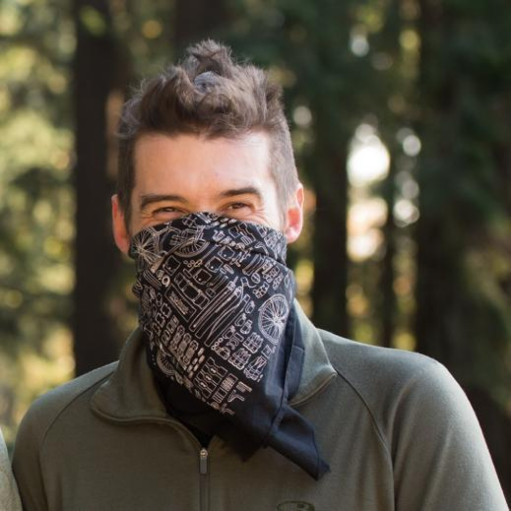 Man wearing a black bandana wrapped around the lower half of his face. The bandana features a variety of bicycle parts are drawn in white and are in a technical style.