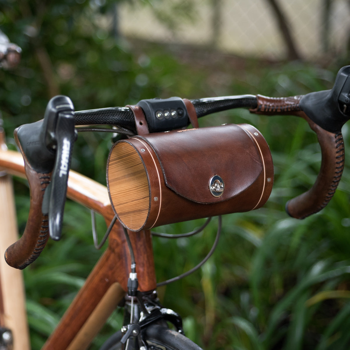 Dark brown leather bicycle barrel bag on handlebars with wood end pieces