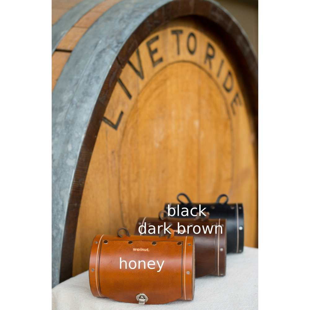 Front view of the three bag color variants: honey, dark brown, and black. The bags are displayed in front of a large barrel that reads &quot;Live to Ride&quot;