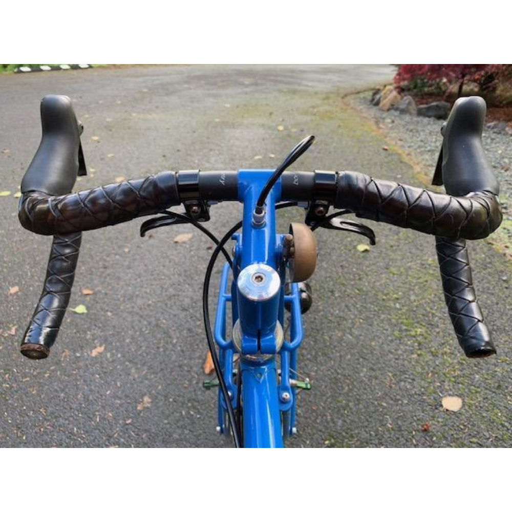 Blue bicycle looking at handlebars as if sitting on the saddle. Handlebar is wrapped in black leather braided wrap.