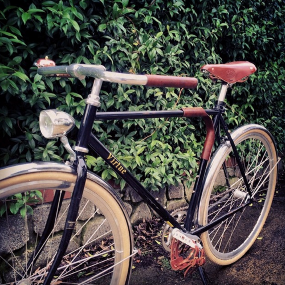 Customer photo of a classy, vintage looking black bicycle with white tires and dark brown leather accessories: Brooks saddle, portage strap, and handlebar grips. 