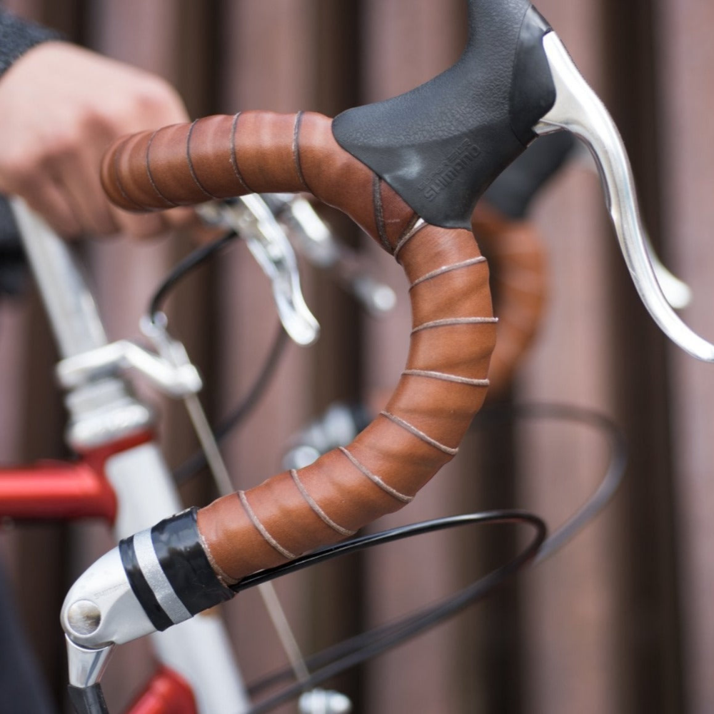 Close-up view of dark brown coiled leather bar tape on bicycle drop bars with brake hoods