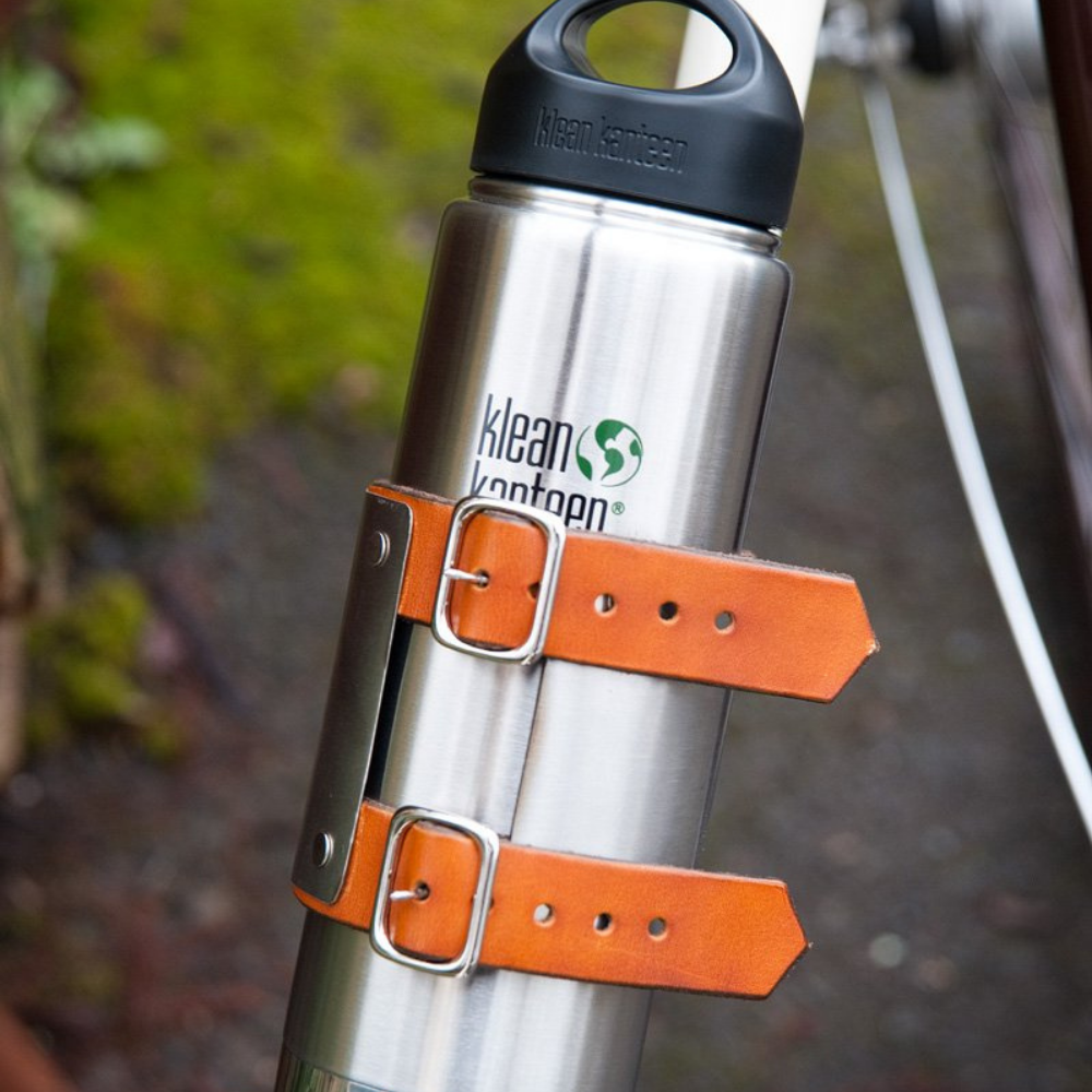 Close-up back view of klean kanteen water bottle attached to white bicycle frame with honey leather straps