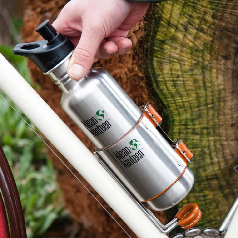 klean kanteen branded water bottle resting in the upcycle cage drink holder attached to a white bicycle frame