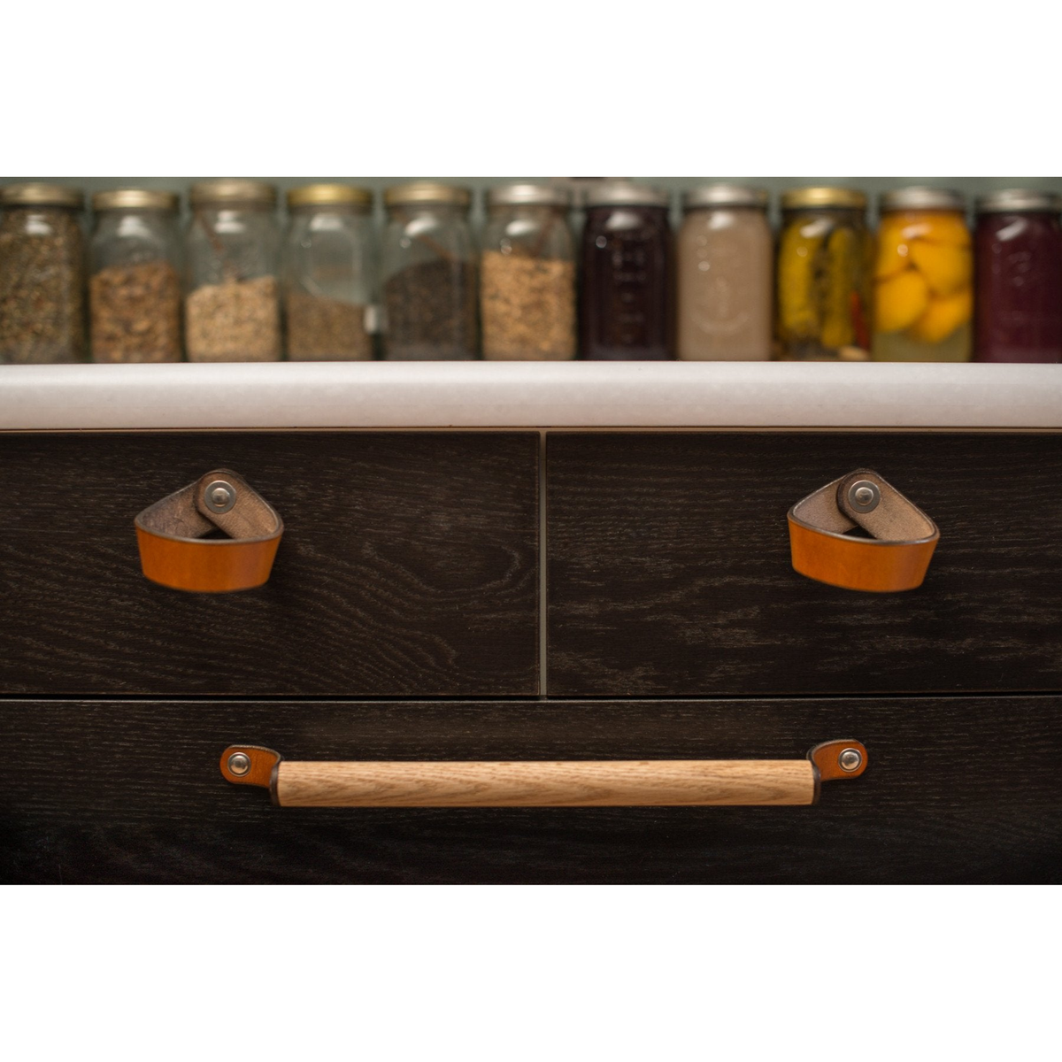 Photo showing the large Sellwood white oak handle against two small drawers with Fremont leather loop handles in honey on dark brown cabinetry