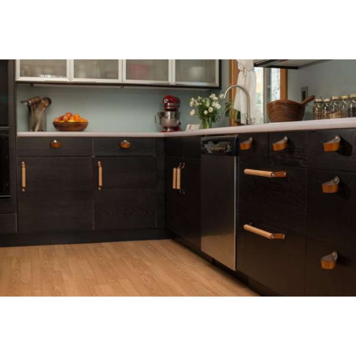 View of an entire kitchen from a distance with black brown IKEA cabinets and honey leather handles. 