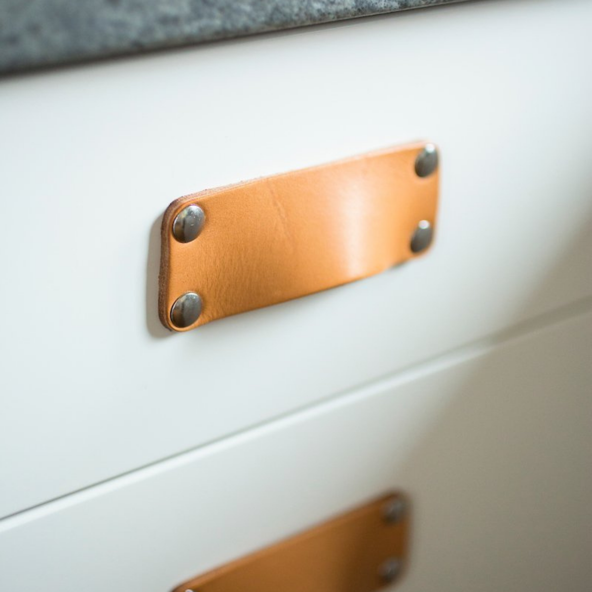 Close-up image of a Natural Morrison leather bin pull with nickel hardware on a white kitchen drawer and a concrete gray kitchen countertop