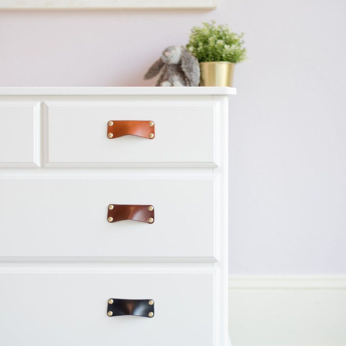 White IKEA HAUGA Chest of Drawers with the Walnut Leather Bin Pull installed in three different colors like an ombre rainbow, growing darker towards the floor.