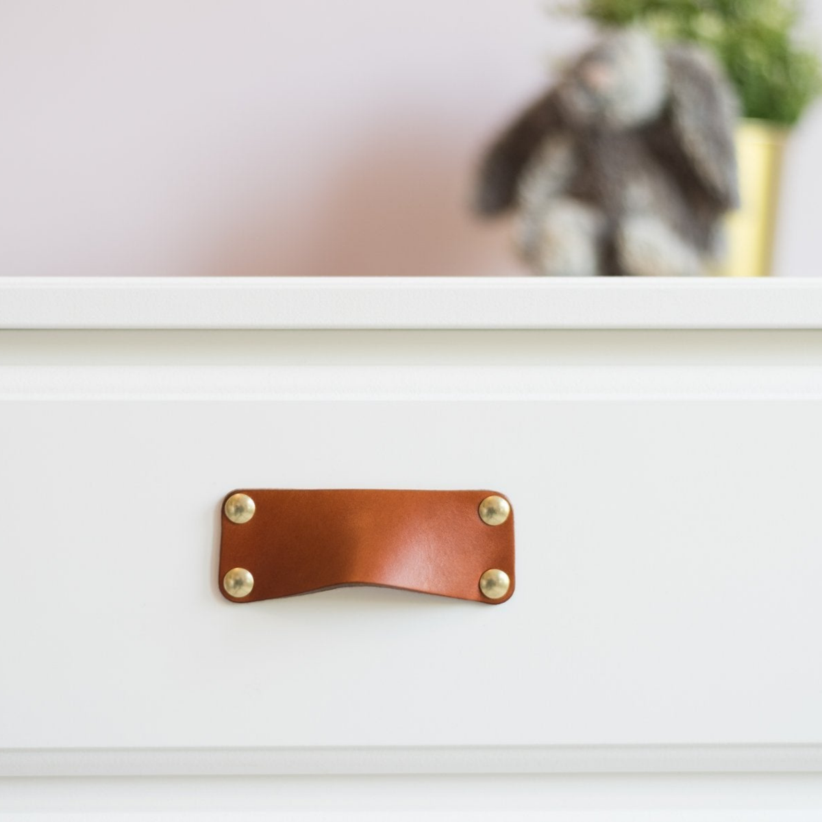 Close-up view of the honey leather bin pull on a white drawer, faced head-on, to see the brass hardware