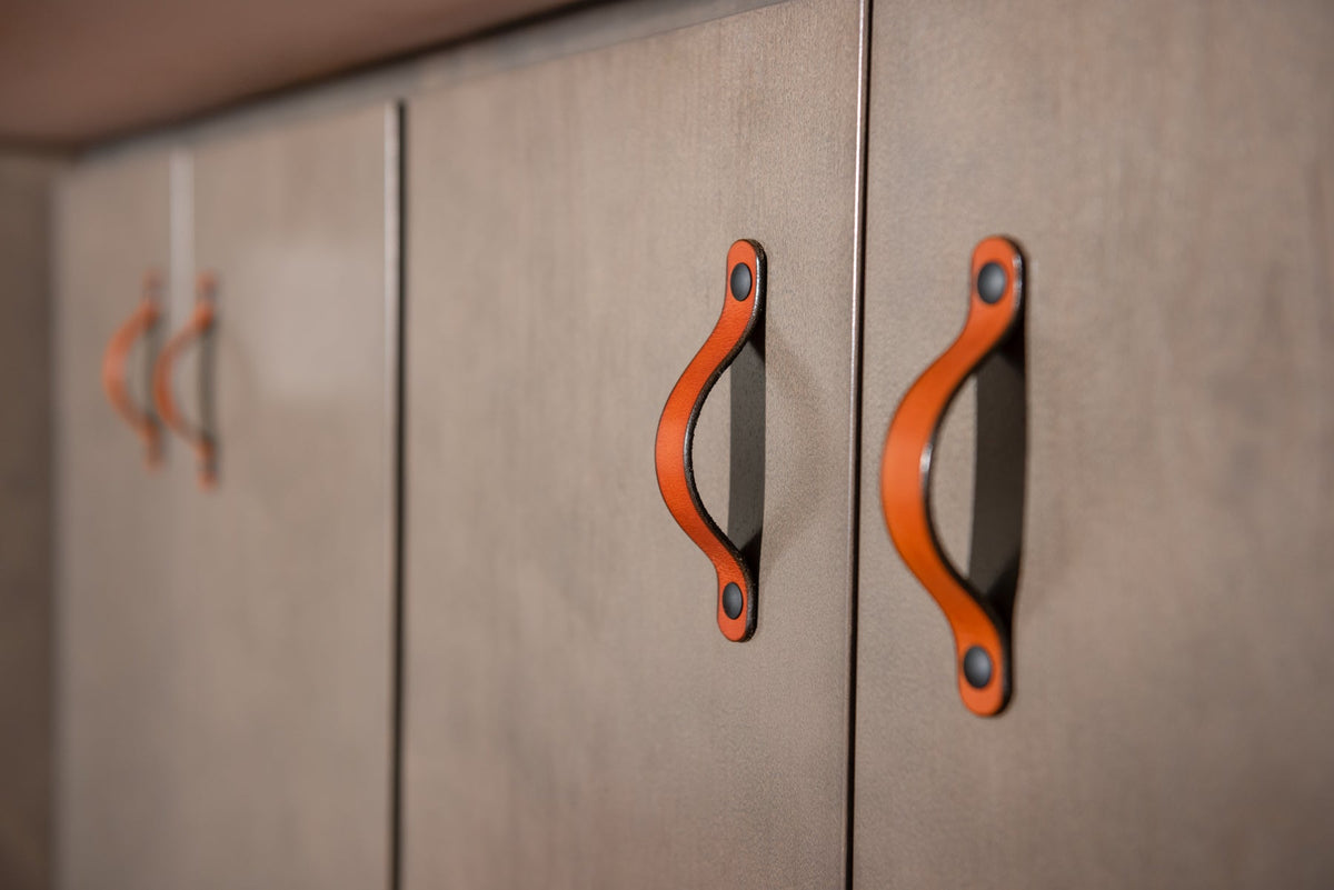 close-up photo of honey leather Flanders handles with black hardware on green cabinets in a line