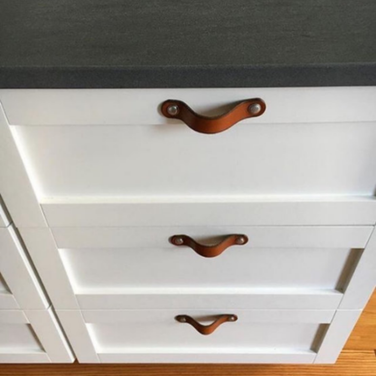 Customer photo looking down a series of white kitchen drawers from standing at the countertop. Each drawer has a small Hawthorne leather handle installed flat with two sets of hardware. 