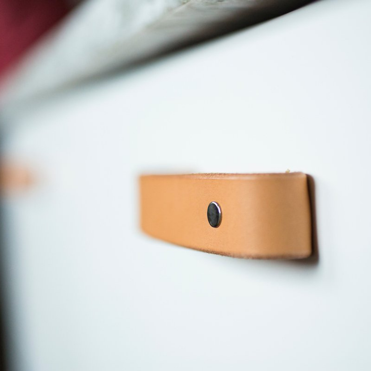 Close-up view of the Tilikum Natural leather handle with Black hardware on a white kitchen drawer. 