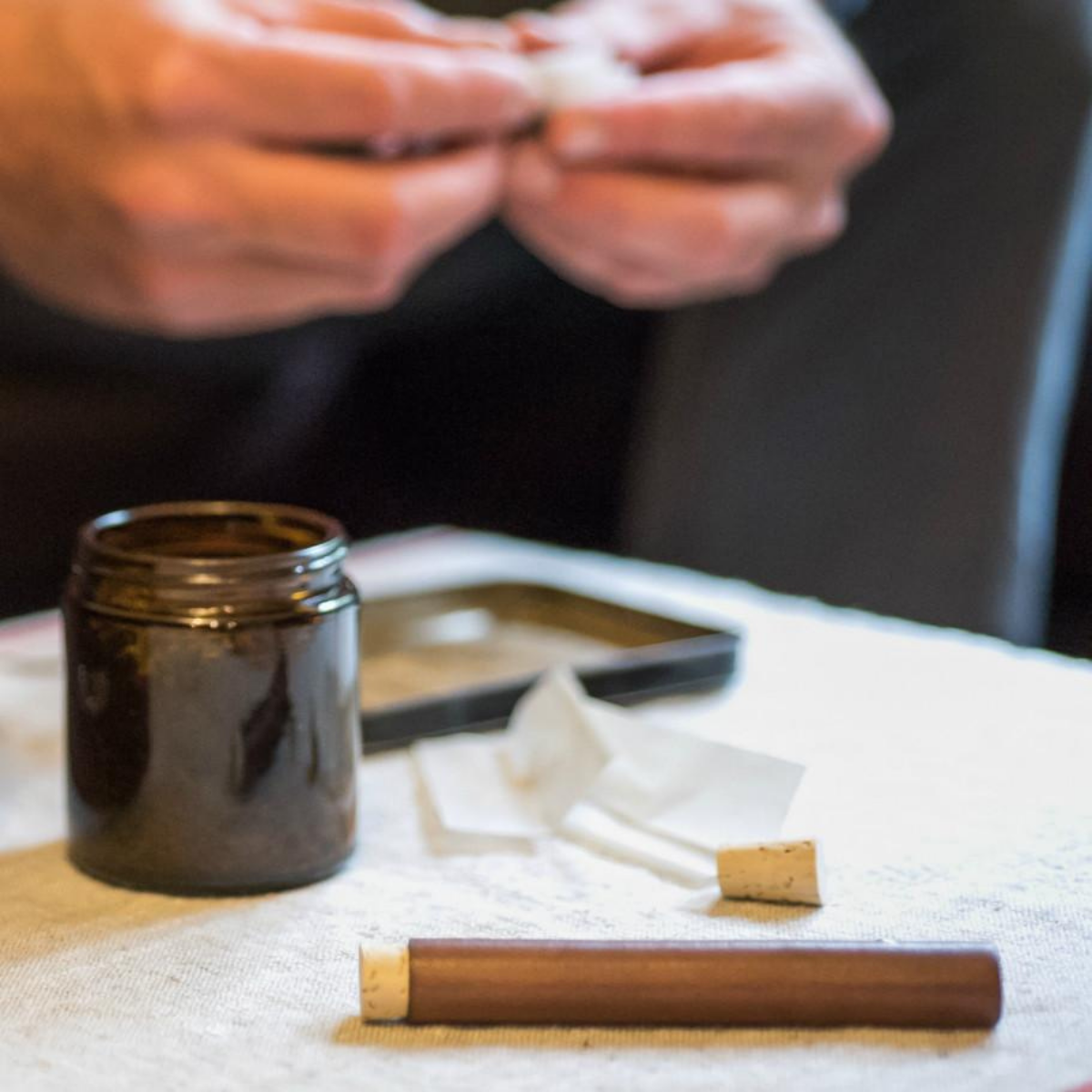 Capless handroll cigarette tube next to glass jar of herbs and rolling tray