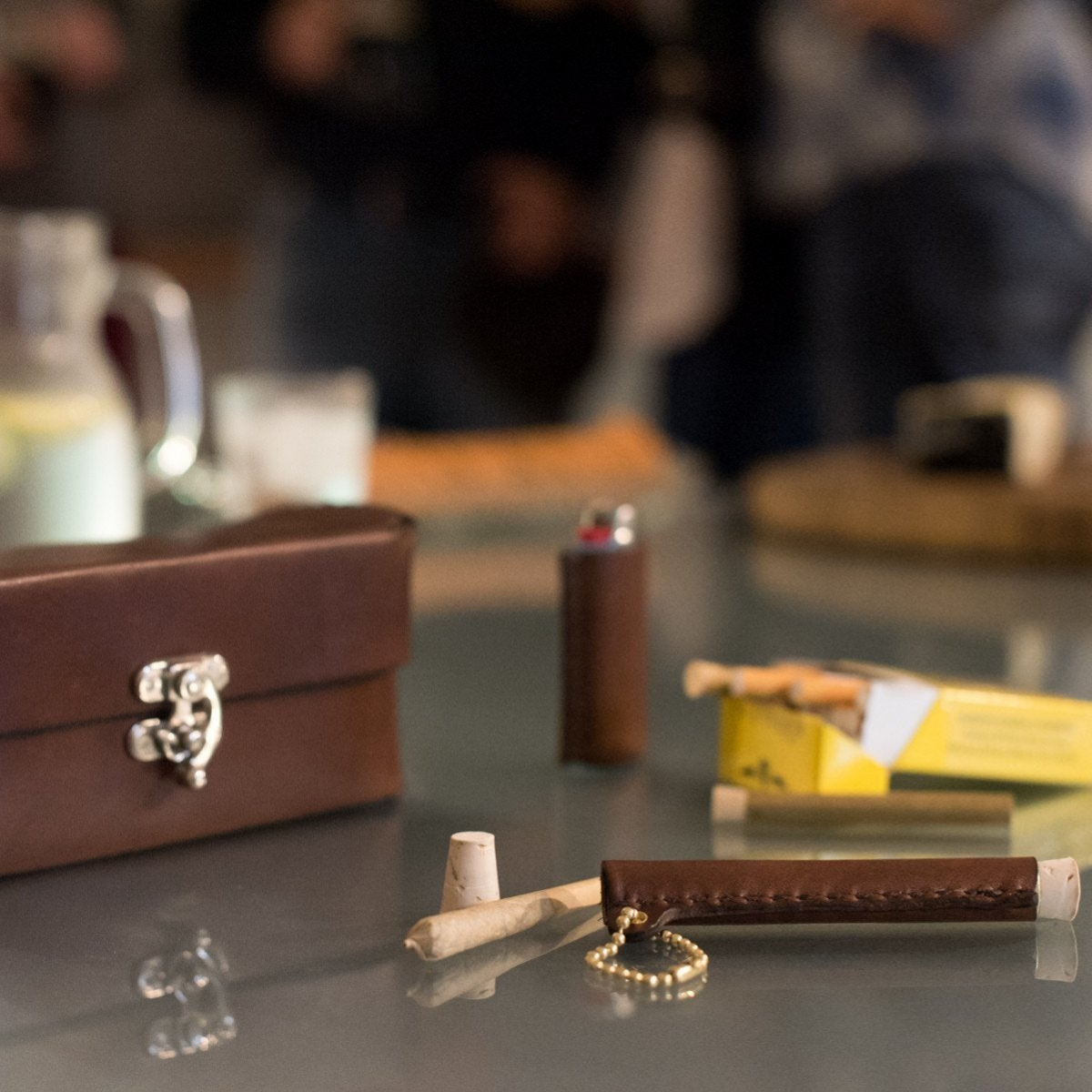 Dark brown genuine leather cigarette case, herbal cigarette holder, and lighter case displayed on a glass table