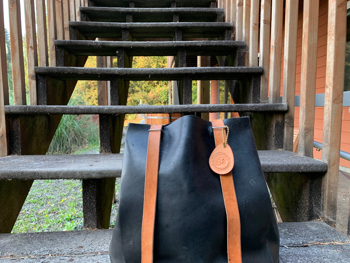 Leather backpack on a set of stairs outdoors with a leather Artisans Cooperative keychain attached to the strap as a bag tag. 