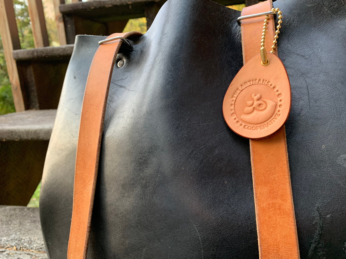 Close-up of leather backpack on a set of stairs outdoors with a leather Artisans Cooperative keychain attached to the strap as a bag tag.