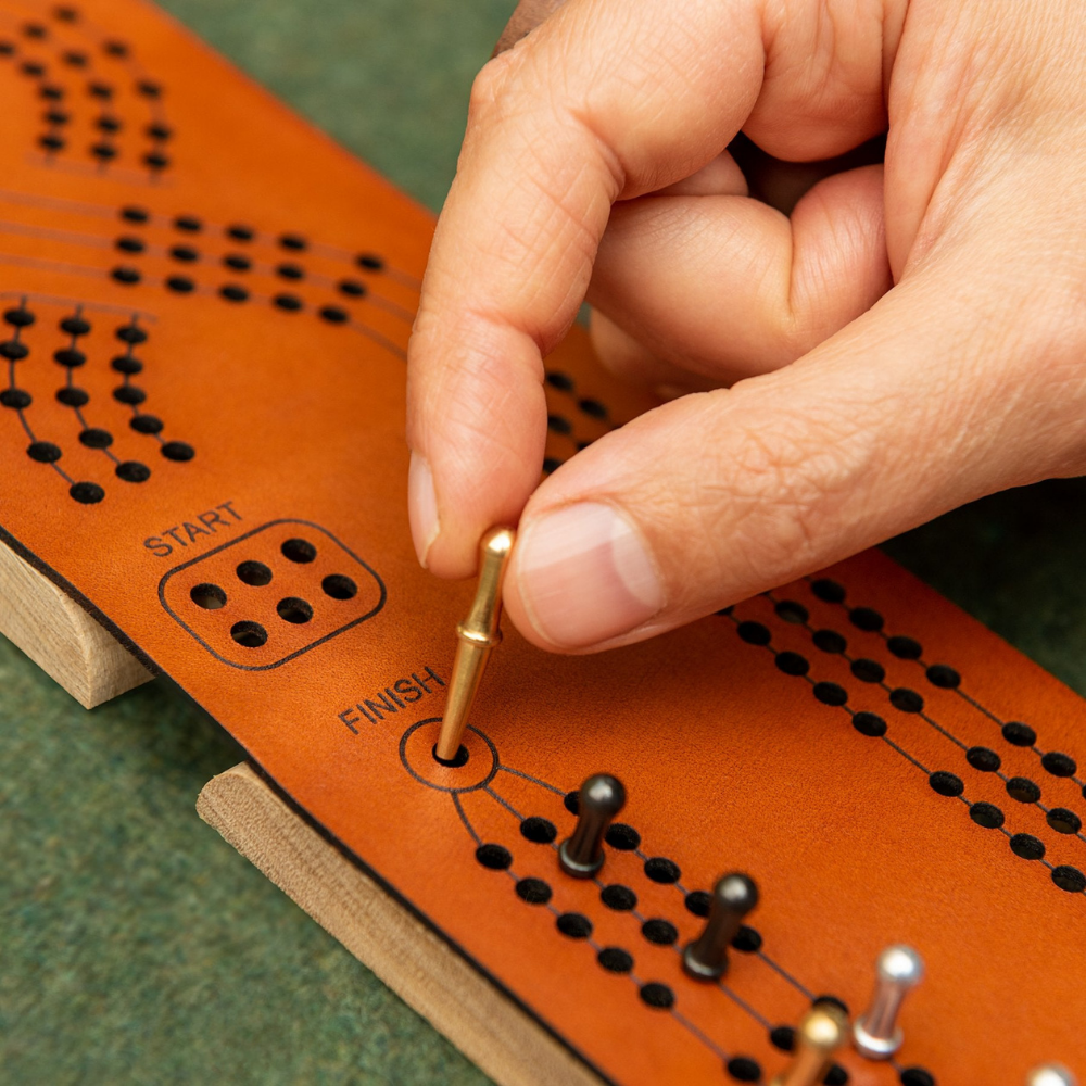 Close-up of Hand Holding Small Brass Pegs in Cribbage Board Set with Black, Silver, and Brass Pegs