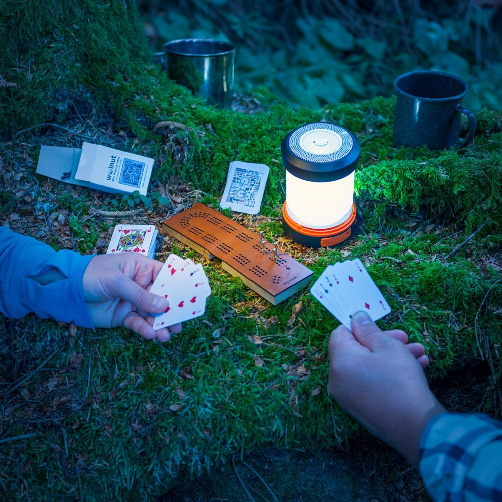 Playing cribbage at night while backpacking on a leather folding travel cribbage board in the forest with a cup of tea