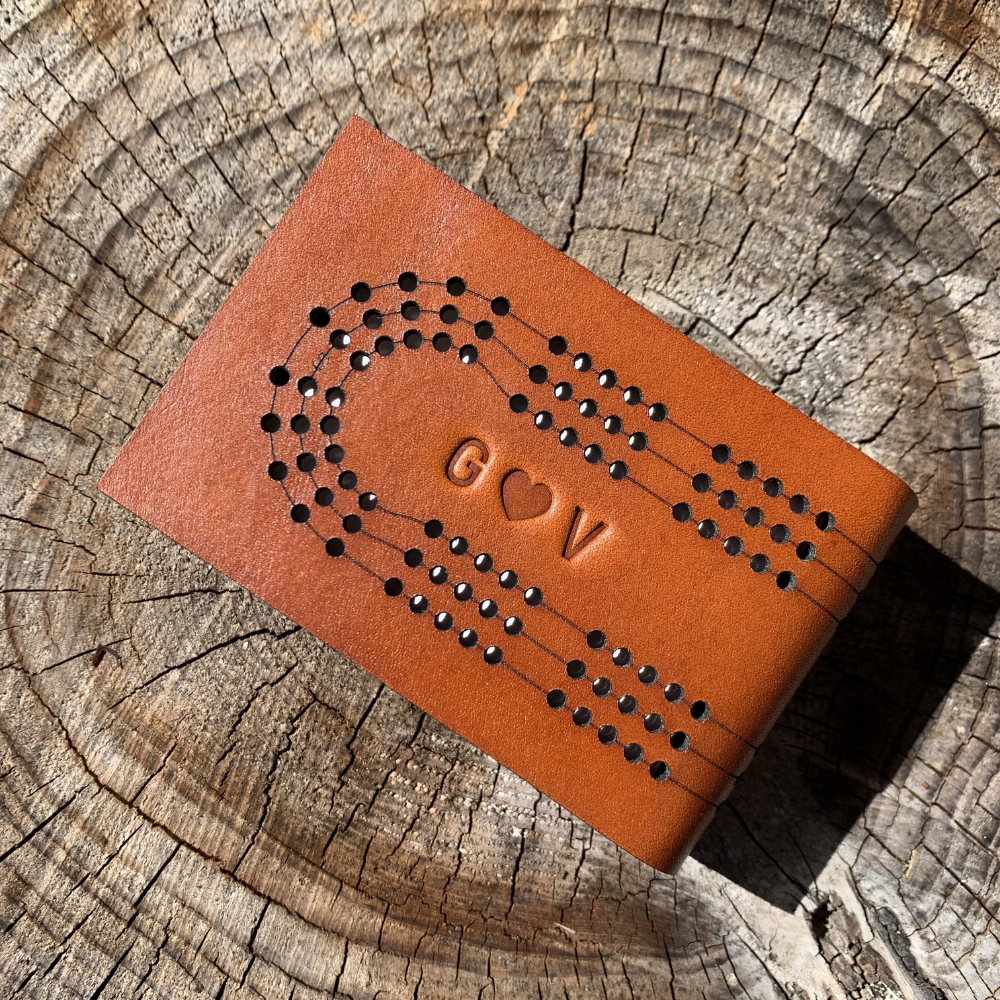 Close-up of monogrammed leather travel cribbage board showing initials and a heart on top of a tree stump