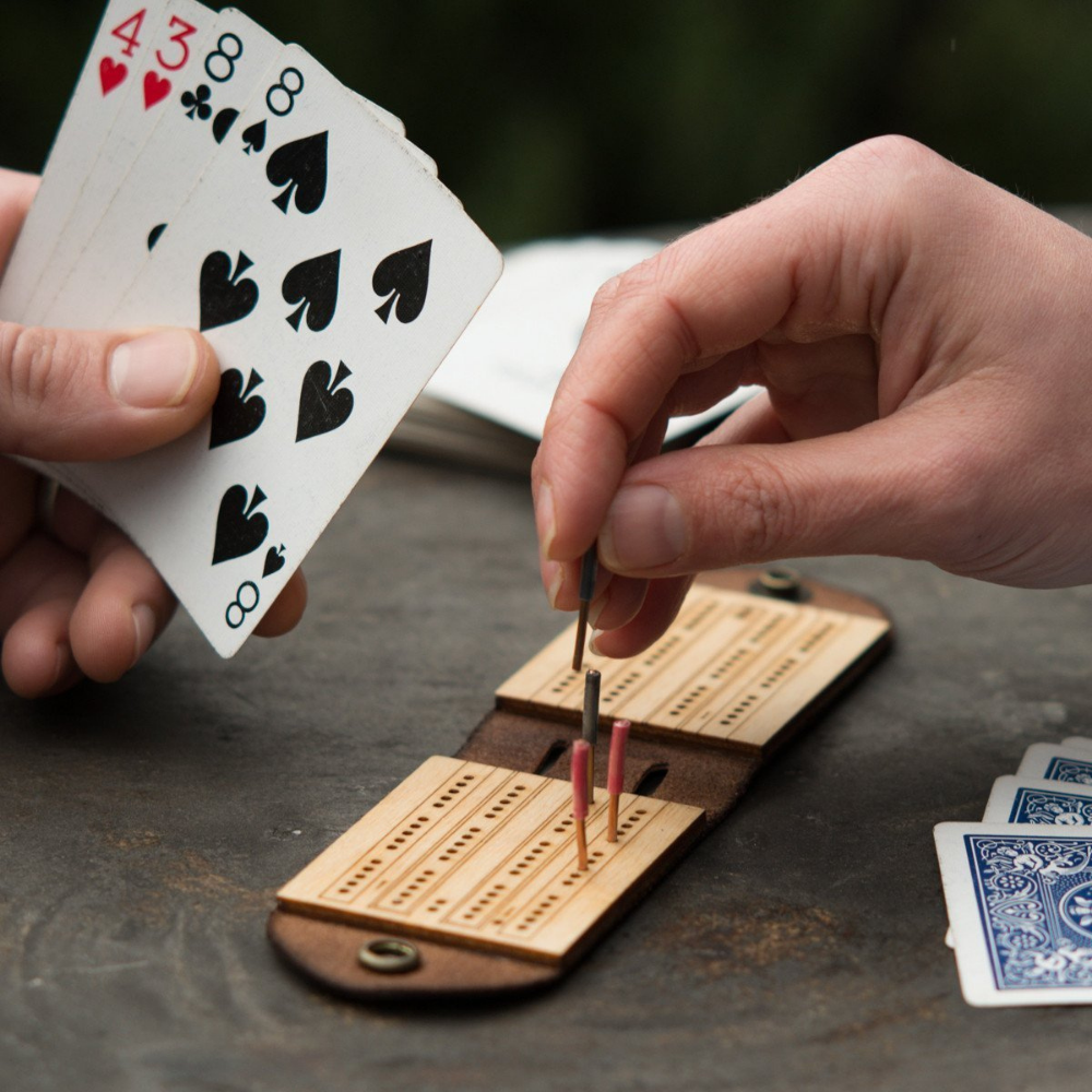 Two people playing on a small, foldable, wood and leather travel cribbage board