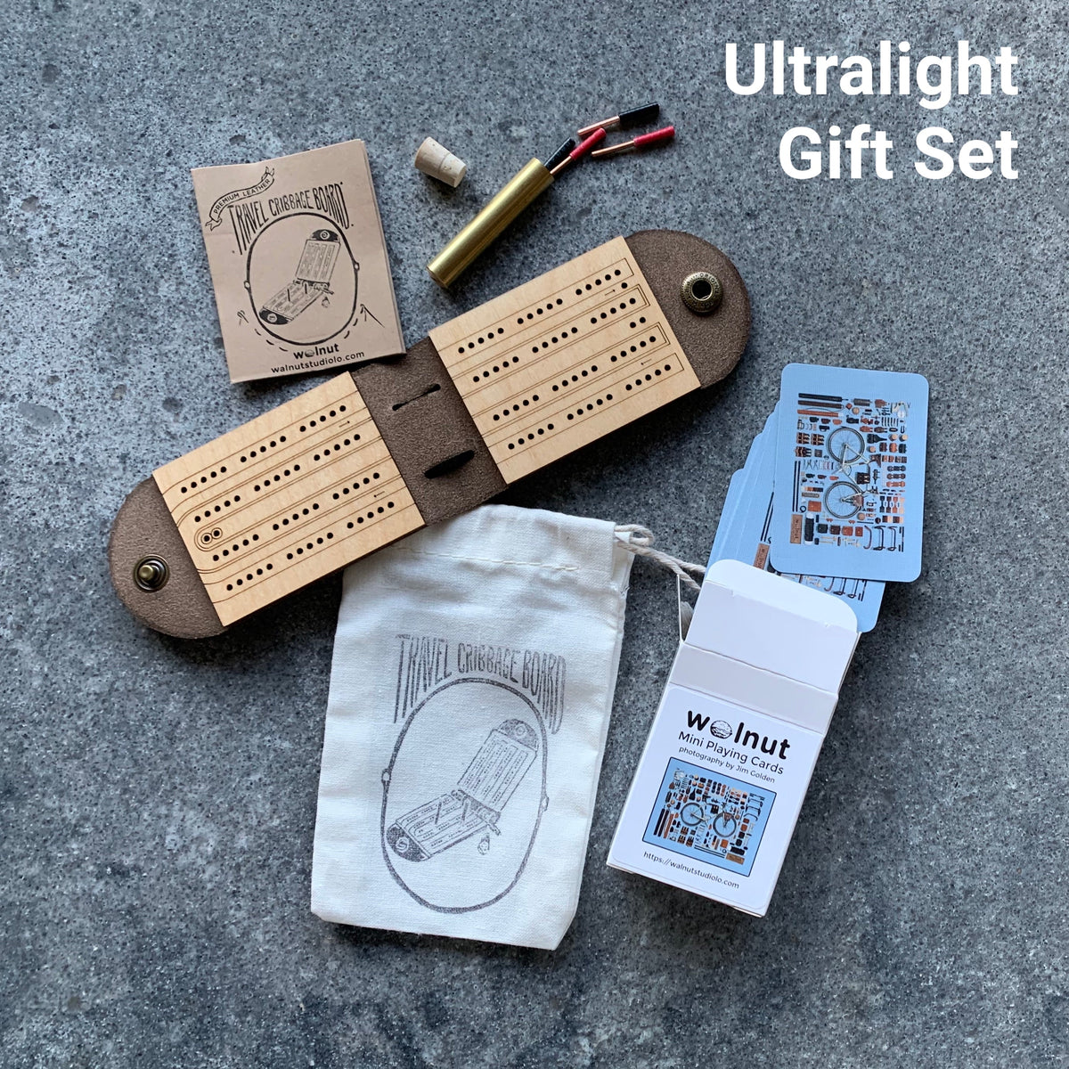 Open leather and wood travel cribbage board with wire metal pegs on a tabletop with a carrying pouch and a half-sized deck of cards, which is the &quot;Ultralight Gift Set&quot;